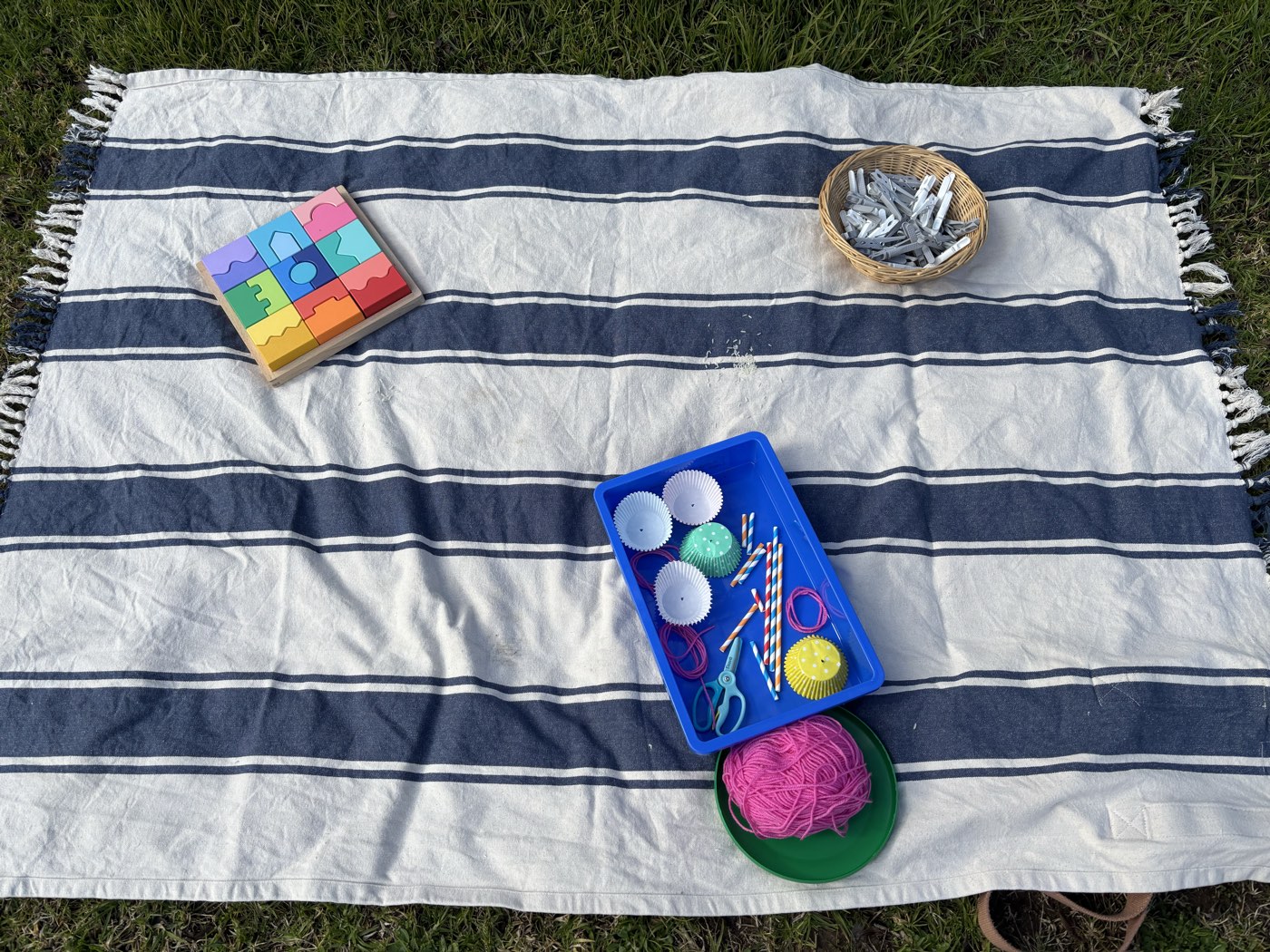 A craft morning laid out on a picnic rug, with yarn, threading tools, and a wooden puzzle