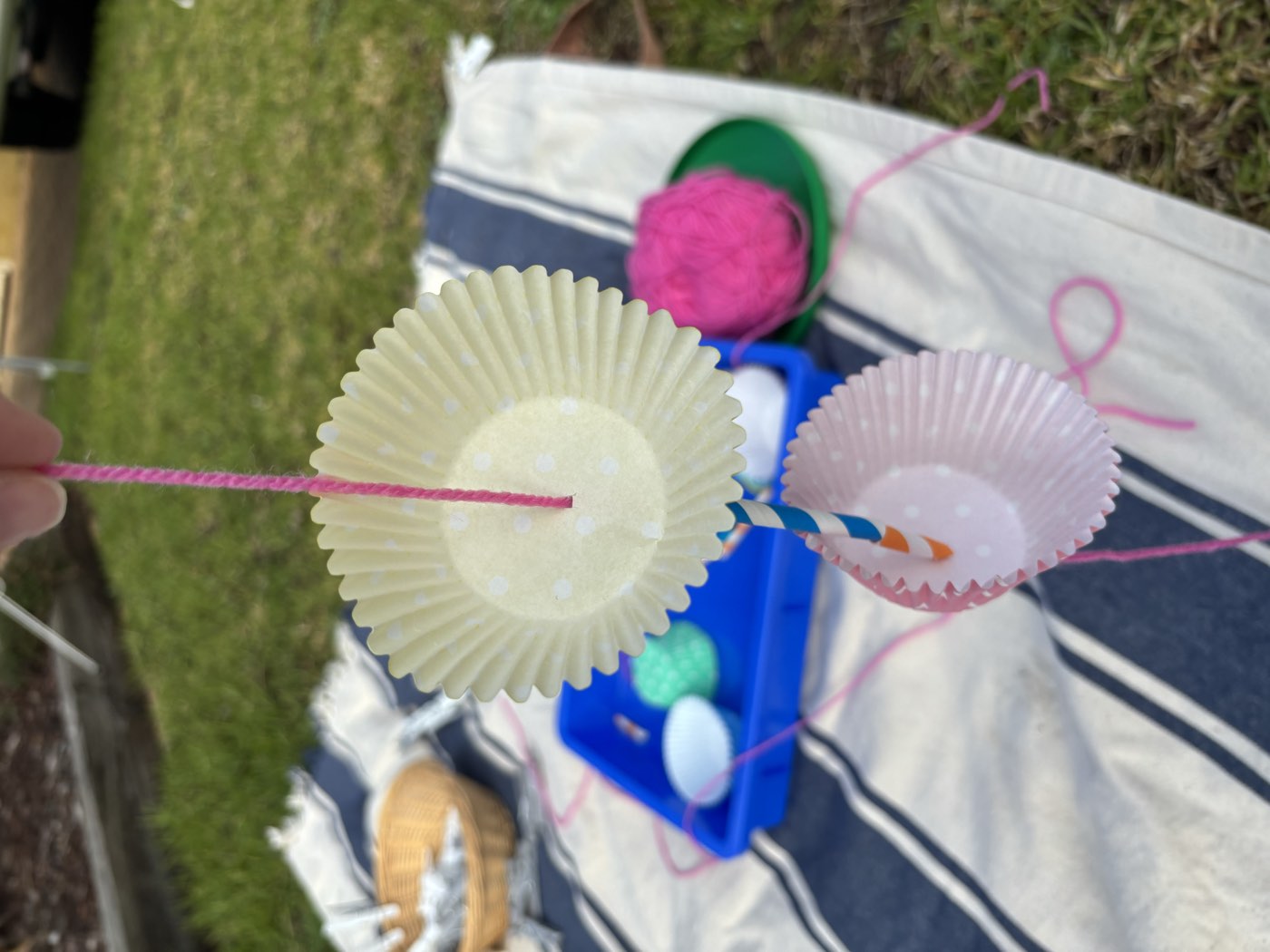 A threading craft in progress, with paper cases and a striped straw on bright pink yarn